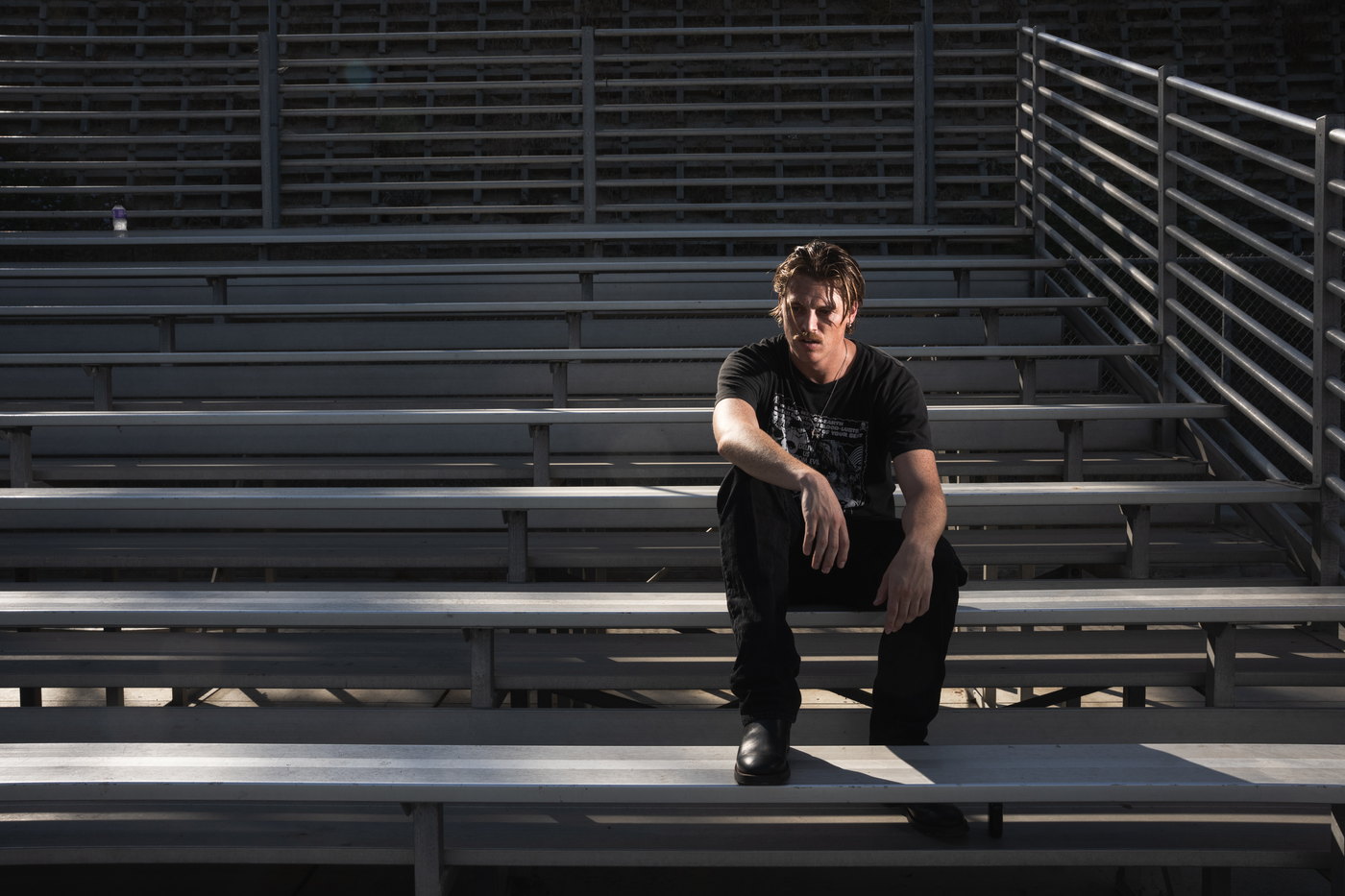 campthehills sitting alone on empty aluminium bleachers in hard afternoon sunlight.